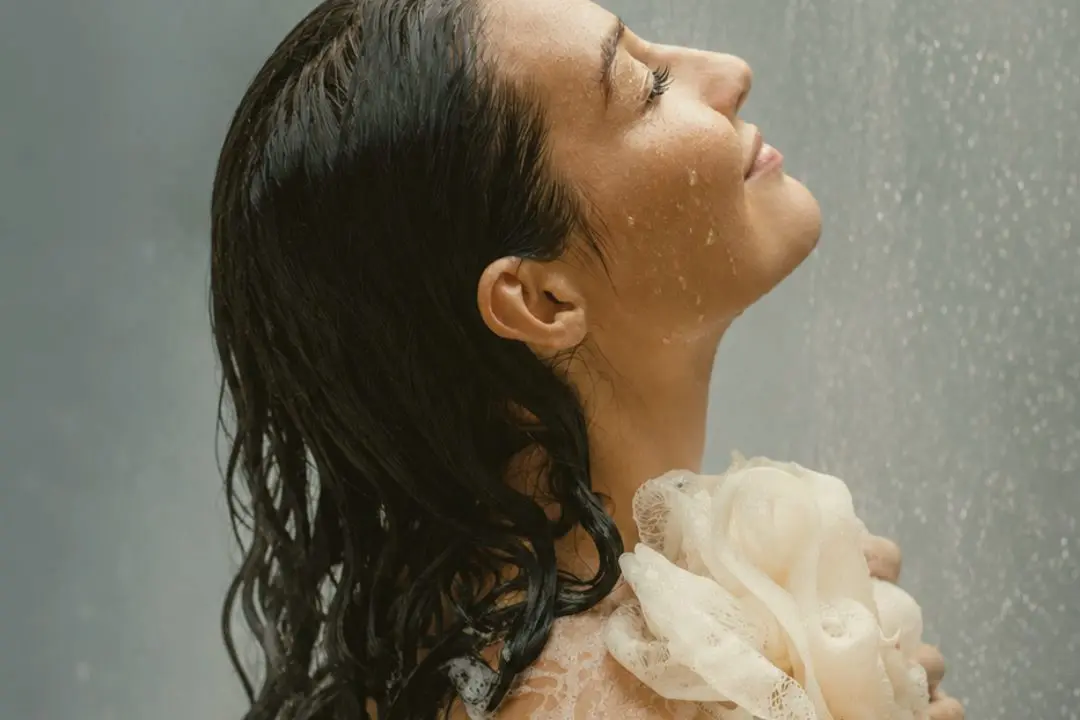 A woman tilts her face into the shower